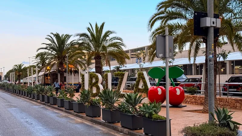 Ibiza Airport exterior with palm trees, Ibiza sign and arrivals pickup area